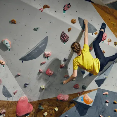 Woman bouldering indoors, stretching mid-climb, showcasing full-body health benefits of climbing sport