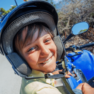 Smiling child wearing a helmet sits on a blue ATV ready for a fun ride