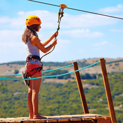 A woman clips into a zipline pulley, preparing for her ride and wondering is ziplining safe