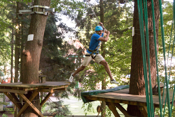 A man enjoys a thrilling ropes course zipline ride through trees, wearing a harness and helmet