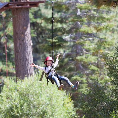 Young boy wearing helmet spreads arms wide while ziplining through a scenic forest adventure course