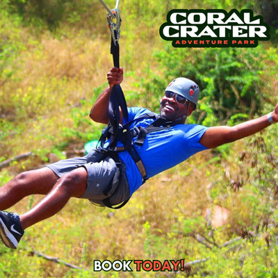 Man in sunglasses and helmet smiles while ziplining at Coral Crater Adventure Park in sunny weather