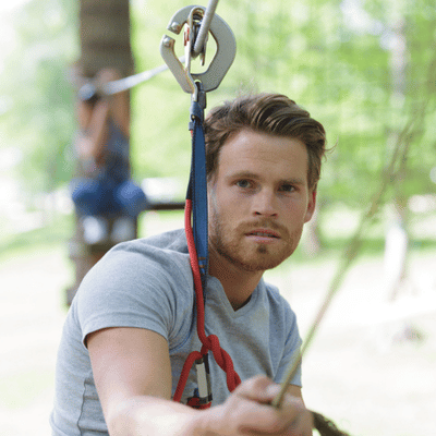 Man prepares for zipline ride, carabiner attached, focusing on safety procedures at outdoor adventure park