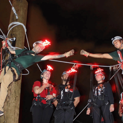 Guides and participants connect on elevated platforms with harnesses during nighttime zipline course high above