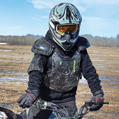 ATV rider in helmet, goggles, and chest armor pauses on muddy field during outing today