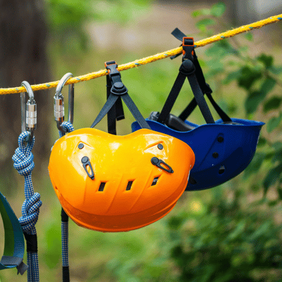 Colorful helmets and clipped carabiners hang from rope, ready for next zipline participants to ride