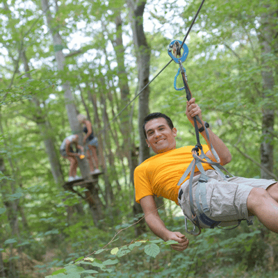 Smiling man glides on forest zipline; guides nearby; asks can you zipline in the rain