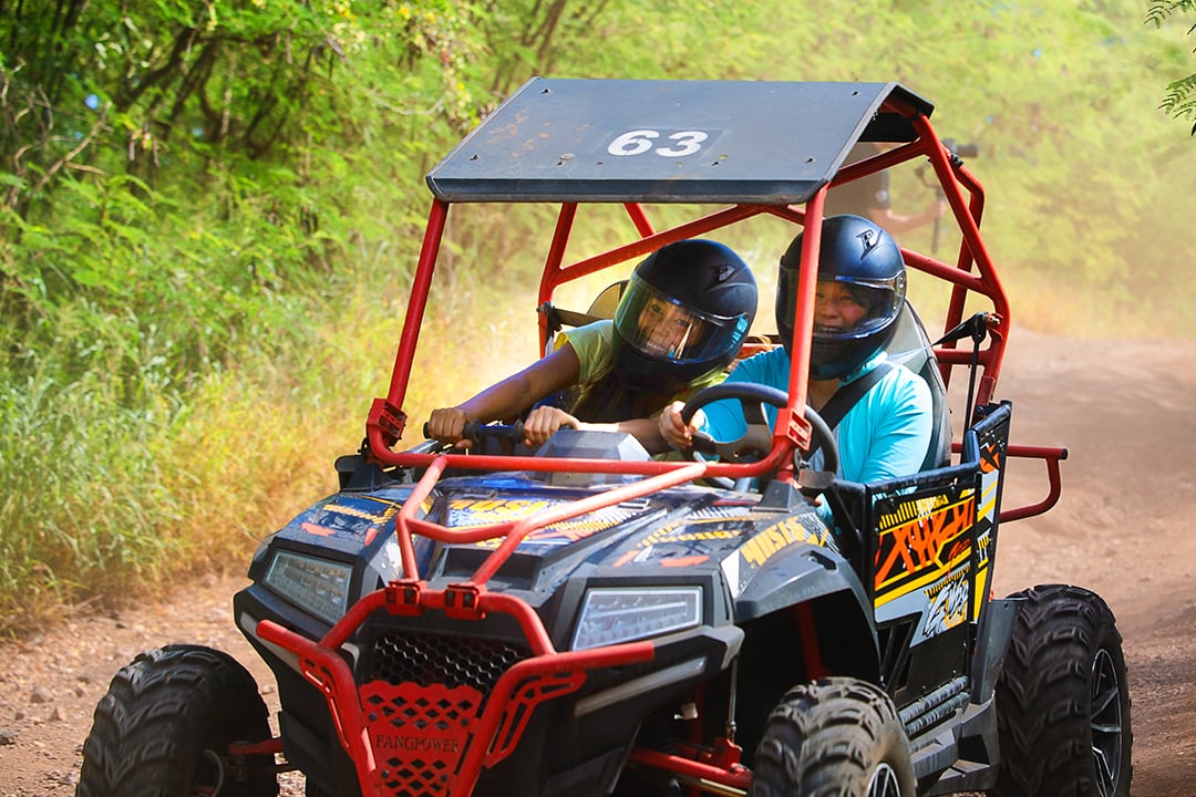 Two young people riding an ATV and smiling at Coral Crater Adventure Park. 